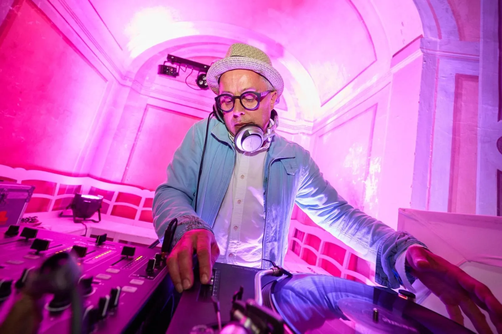 DJ Misha Bender mit Hut, Brille und Kopfhörer an den Plattenspielern in pinkem Licht