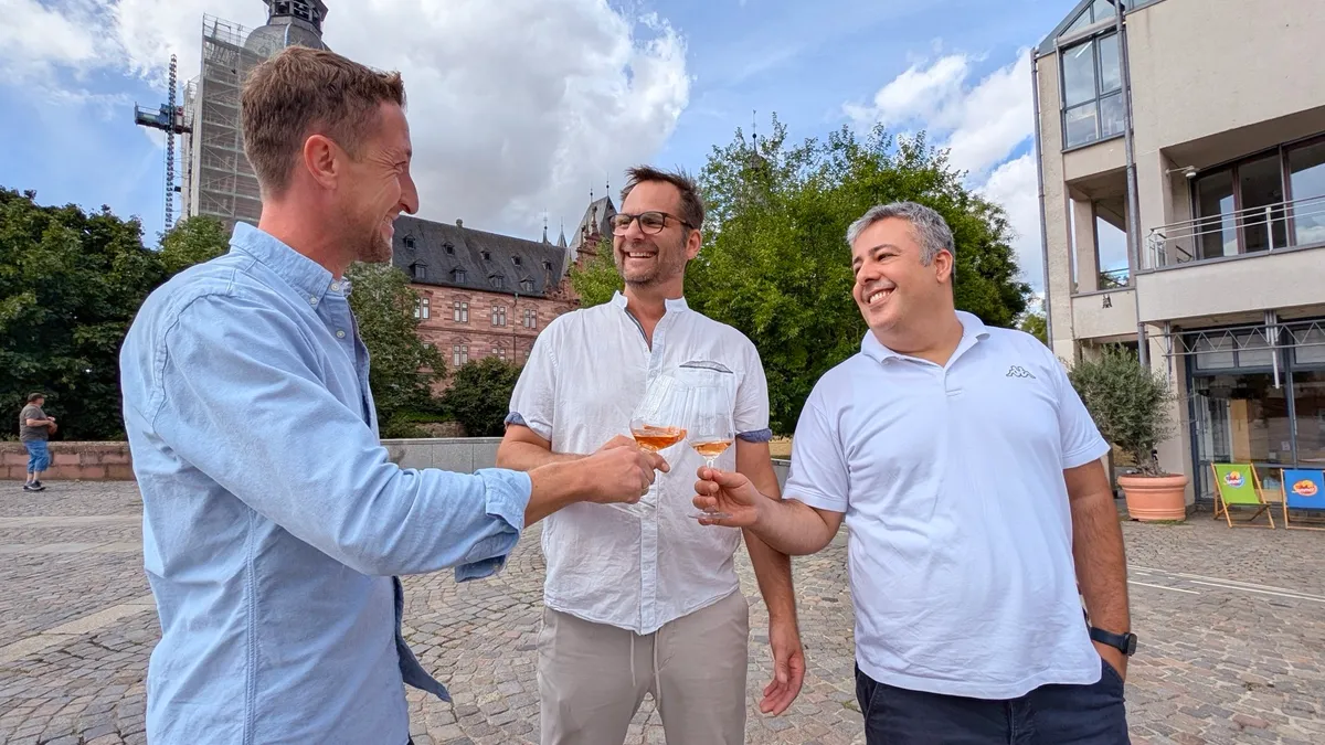 Die drei Veranstalter des Vinum Culinarium stoßen auf dem Schlossplatz an, im Hintergrund Schloss Johannisburg
